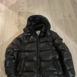 Svart Moncler Maya - Säljer en snygg svart dunjacka från Moncler. Jackan har en pufferdesign med dragkedja och huva. Perfekt för kalla dagar med sin varma och stilrena look. Passar både till vardags och mer uppklädda tillfällen. Storlek 3 passar som M