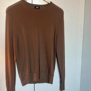 Brun stickad tröja från Uniqlo - En stilren sand brun stickad tröja från Uniqlo i storlek S. Tröjan har rund halsringning, långa ärmar och ribbade muddar vid ärmslut och nederkant. Perfekt för lager-på-lager och enkel att matcha med olika outfits.