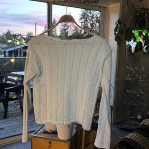 Vit stickad tröja från 157 - Vit stickad tröja från 157 med lång ärm och snyggt hålmönster i ränder över hela tröjan. Tröjan har en rak passform och är perfekt för lager-på-lager. Mjuk och skön känsla, passar till både jeans och kjol.