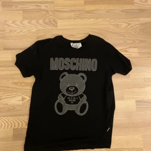 Svart Moschino t-shirt  - Svart t shirt från Moschino med grått tryck. Storlek L men skulle nog säga att den passar bättre på M. Vänligen hör av er vid intresse! 