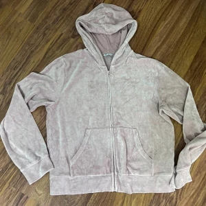 Ljusrosa velour hoodie med dragkedja - Mysig ljusrosa hoodie i velour med dragkedja framtill och stora fickor. Tröjan har huva och långa ärmar, perfekt för chill dagar. Enkel och stilren design som är lätt att matcha med andra plagg.