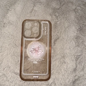 iPhone 14 Pro Skal Bling Bling Pink Bow - Sött genomskinligt skal till iPhone 14 Pro med rosa rosett och text. Skalets skick är använt, med viss missfärgning och repor, men motivet är intakt. Skyddar din mobil och ger en unik, feminin look. Passar perfekt för dig som vill ha ett personligt och stilrent skydd.