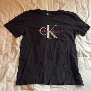 Svart Calvin Klein tröja - Jag säljer min svarta Calvin Klein tröja med vitt och rosa tryck över bröstet. Storlek 16 år motsvarar typ S/M. Köpt från kidsbrandstore. Säljer för den inte kommer till användning.