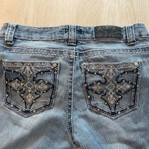Lågmidjade bootcut jeans med detaljer - Ljusblå tunnare jeans från Soundgirl med snygga broderade bakfickor och nitar.                 Innerbens mått: 70 cm                                       Midja rakt över: 36cm                                              Defekter: Lite nötta på ena knät .                         Byter även mot ett annat par jeans om det är intressant!                                                                Pris kan diskuteras vid snabb affär!