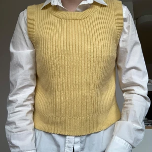 Gul stickad väst från Monki - Superfin ribbstickad väst i ljusgul färg från Monki. Modellen är ärmlös med rund halsringning och har en klassisk, rak passform. Materialet är en mix av bomull och akryl som gör den både mjuk och bekväm. Perfekt att styla över skjorta för en trendig look.