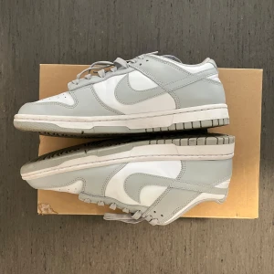 Nike Dunk Low grå/vita sneakers - Nike Dunk Low sneakers i  grå och vit färg. Skorna är helt ny. Använda 4 gånger. Har veck vid sidan på en av skorna.