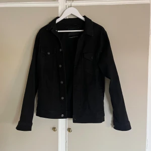 Svart jeansjacka från Zara, stl S - Stilren svart jeansjacka från Zara i klassisk modell med knappar framtill och bröstfickor med lock. Jackan har lång ärm och är tillverkad i ett tåligt denimtyg. Perfekt för dig som gillar en clean och tidlös look.