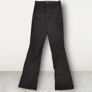 Svarta bootcut kostymbyxor Zara - Svarta kostymbyxor från Zara med bootcut-silhuett och klassiska pressveck. Byxorna har hällor för bälte och stängs med dold dragkedja och hake. Perfekta för en clean och stilren look.