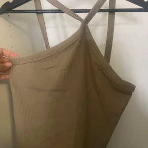 Beige ribbad linnetopp Gina Tricot - Säljer en beige ribbad linnetopp från Gina Tricot i storlek S. Toppen har smala axelband som korsas i ryggen och en enkel, stilren design. Perfekt att matcha med jeans eller kjol för en chill look.