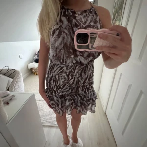Brun och vit kortklänning med volang - Säljer en snygg kortklänning i brunt och vitt med zebramönster. Klänningen är ärmlös, har en luftig passform upptill och smockad midja. Nederdelen har en volangkant som ger extra rörelse. Tunt, lätt material som känns perfekt för varmare dagar. Så trendig!!