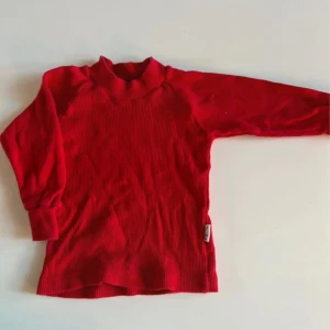 Röd ribbad polotröja från Joha - Röd polotröja från Joha i ribbad design. Tröjan har lång ärm och hög krage, perfekt för lager-på-lager. Tillverkad i mjukt material som känns skönt mot huden. Enkel och stilren modell som funkar till många outfits.