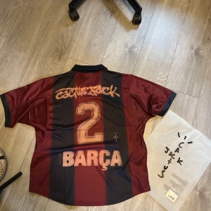Barça x Cactus Jack x Nike fotbollströja - ÄNDA ORGINALET PÅ SVENSKA MARKNADEN!Unik Barcelona fotbollströja i samarbete med Cactus Jack och Nike. Tröjan är kortärmad med klassiska blå och vinröda ränder, tryckta detaljer som 'Cactus Jack', nummer 2 och 'BARÇA' på ryggen samt klubbmärke och Nike-logga på bröstet. Materialet är glansigt och lätt, perfekt för fotboll eller streetwear. Självklart original, och köpbevis finns att uppvisa. 