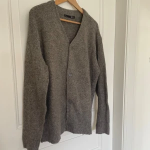 Grå kofta från 157 i ullmix - Mysig grå kofta från 157 i storlek M. Koftan är stickad med ribbade muddar och knäpps med knappar framtill. Perfekt för lager-på-lager och chill höst- och vinterstil.