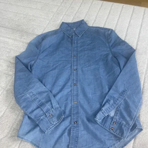 Blå jeansskjorta från Diker Style - Snygg blå jeansskjorta från Diker Style med klassisk krage och knäppning framtill. Skjortan har långa ärmar och är tillverkad i mjukt jeanstyg. Perfekt för en avslappnad och cool look.