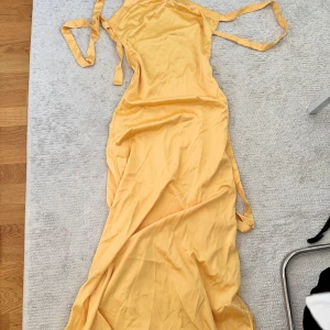 Gul långklänning från Do My Self - Snygg gul långklänning med öppen rygg och knytband i sidorna. Klänningen har en slimmad passform och är tillverkad i ett lätt, mjukt material som känns svalt mot huden. Perfekt för varma dagar och somriga vibes.