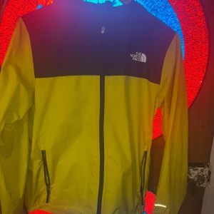 Gul och svart vindjacka The North Face - Snygg gul och svart vindjacka från The North Face med hel dragkedja framtill och två fickor med dragkedja. Jackan har lång ärm med reflekterande detaljer och logga på bröstet och ärmen. Perfekt för blåsiga dagar och streetstyle. Kan diskutera pris 