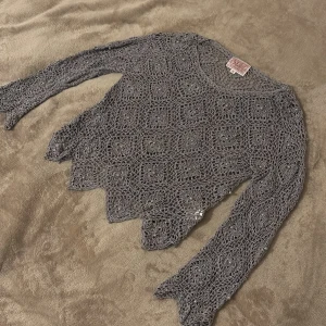 Grå virkad blus med pärldetaljer - En vacker långärmad blus med spetsig nederkant och ett noggrant virkat mönster av rutor, där varje ruta pryds av en liten pärla för extra elegans. Perfekt för dig som älskar en bohemisk, romantisk och kreativ stil ✨  ✔️ Unik design – sticker verkligen ut ✔️ Detaljerade virkade rutor med insydda pärlor ✔️ Lätt att styla till både vardag och fest  💸 Jag säljer många fina plagg billigt – kika gärna på min sida för fler fynd! 🤝 Jag brukar även acceptera prisförslag, så tveka inte att skicka ett bud.  📦