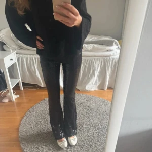 Svarta paljettbyxor med bootcut - Glittriga svarta byxor med paljetter och bootcut-modell. Hög midja och figurnära passform upptill som släpper ut vid benen. Perfekta för dig som vill sticka ut och glänsa lite extra. Materialet är syntet med massor av paljetter för en riktigt festlig look.🖤🌟🎊🎊🎊
