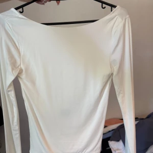 Vit långärmad topp med öppen rygg - Säljer en stilren vit långärmad topp med snyggt djup, öppen rygg. Toppen har en tight passform och är tillverkad i mjukt bomullsmaterial. Perfekt för dig som gillar minimalistisk och clean stil med en twist.