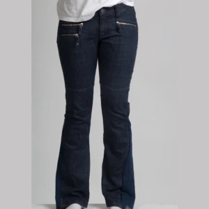 Mörkblå jeans med dragkedjor - Snygga mörkblå jeans med bootcut passform och coola dragkedjor både fram och bak. Jeansen har en klassisk femficksdesign och är tillverkade i ett robust denimtyg. Perfekta för dig som gillar detaljer och vill sticka ut lite extra. För referens är modellen på byxorna 166 cm.