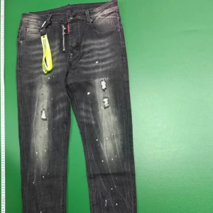 Svarta Dsquared2 jeans med slitningar - Snygga svarta jeans från Dsquared2 med coola slitningar och blekta detaljer. Jeansen har vita färgstänk och klassisk femficksdesign. De är raka i modellen och har en modern streetkänsla. Materialet är jeans i bomull med stretch för extra komfort.