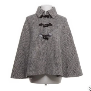 Grå kappa med fiskbensmönster - Stilren grå kappa i fiskbensmönster med snygga knäppningar framtill. Kappan har en klassisk krage och är tillverkad i ett ulligt material som ger en lyxig känsla. Perfekt för dig som vill ha en tidlös och trendig look.