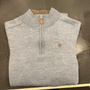 Grå merinoulltröja från Morris - Snygg grå stickad tröja från Morris i 100% merinoull med halv dragkedja och kontrastfärgad brun insida på kragen. Broderad logga på bröstet och ribbade muddar. Perfekt för lager-på-lager under kyliga dagar.