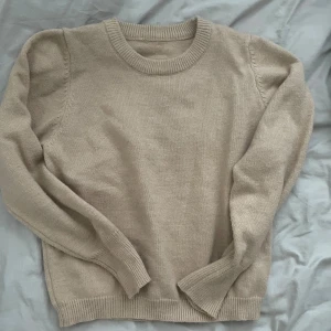 Beige stickad tröja med rund hals - En stilren beige stickad tröja med rund halsringning och ribbade muddar vid ärmslut och nederkant. Perfekt för lager-på-lager och enkel att matcha med olika outfits.