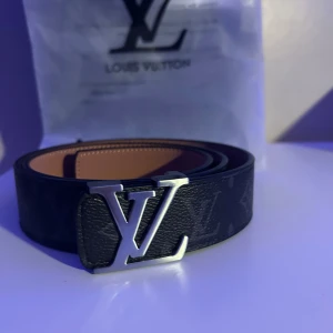 Monogram bälte - Snyggt svart bälte L—V med klassiskt monogram och silverfärgat spänne. Bältet helt nytt  mig och har bara svarta ränder på insidan från fabrik men det syns inte 