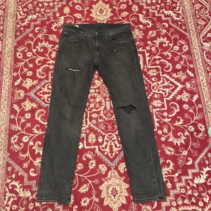 Levi's 502 slitningar - Svarta Levi's 502 jeans med raka ben och snygga slitningar på låren och knät. Klassisk femficksmodell med läderpatch bak i midjan och röd Levi's-tagg på bakfickan. Jeansen är i denim och har en modern, avslappnad look.