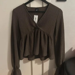 Brun omlott blus från Gina Tricot - Säljer en brun blus från Gina Tricot i storlek XS. Blusen har omlott-design, v-ringning och volang nedtill. Materialet är strukturerat och känns mjukt mot huden. Långa ärmar med lätt puff och resår vid ärmslut ger en snygg siluett.