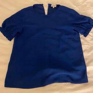 Blå blus  - Säljer en snygg blå blus med korta puffärmar och rund halsringning.  Blusen har en enkel och stilren design, aldrig använt