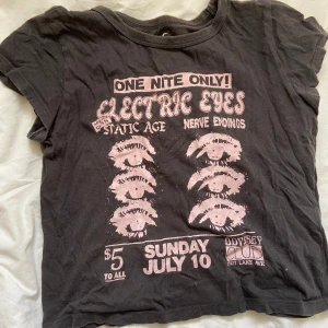 Svart t-shirt från Hollister - Svart t-shirt från Hollister med coolt rosa tryck framtill. Trycket har text och ögonmotiv i vintage-stil. T-shirten är i 100% bomull, har rund hals och korta ärmar. Perfekt för dig som gillar en edgy och avslappnad look. Jag säljer den nu på grund av att den inte är i min stil längre. Kan förhandla om pris💗