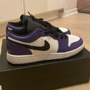 Nike Air Jordan 1 Low Court Purple - Säljer ett par Nike Air Jordan 1 Low i färgen Court Purple. Skorna har en snygg kombination av vitt, lila och svart skinn, klassisk svart swoosh och svart snörning. Ikoniska Jordan Wings-loggan på hälen och perforerad tå för extra stil. Perfekta för dig som vill sticka ut. Helt nya!!!!