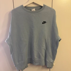 Ljusblå sweatshirt från Nike - Säljer en ljusblå sweatshirt från Nike med klassisk logga broderad i svart på bröstet. Tröjan har rund halsringning och långa ärmar, perfekt för en chill och sportig stil. Mjuk och skön bomullskänsla.