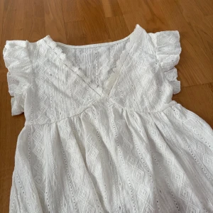 Vit tröja från SHEIN - Superfin vit tröja från SHEIN med v-ringning, volangärmar och broderade detaljer. Klänningen har ett romantiskt mönster och är gjord i bomullsmix, perfekt för sommarens varma dagar. Söt och luftig modell med omlottkänsla upptill.