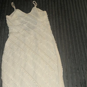 Krämvit ribbad långklänning - Superfin krämvit långklänning maxi med smala axelband och ribbad struktur. Klänningen har ett diskret mönster i tyget och en lätt figurnära passform. Perfekt för varma dagar och somriga vibes.