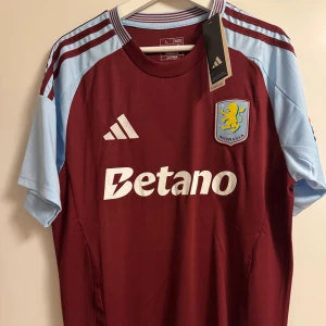 Aston Villa fotbollströja  - Lag och säsong: Aston Villa 2024/2025 Namn: Inget Storlek: L Skick: Oanvänd med lapp kvar. Reprint