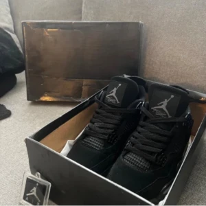 Svarta Nike Jordan 4 sneakers - Säljer ett par svarta Nike Jordan 4 sneakers med klassisk Jumpman-logga på plösen och innersulan. Skorna har snörning, meshpaneler och detaljer i mocka för en clean och sportig look. Kommer med originalkartong och tag. Perfekt för dig som gillar streetwear.