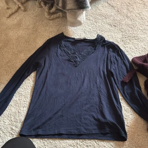 Mörkblå långärmad topp med spets - Snygg mörkblå långärmad topp från Gina Tricot med v-ringad hals och dekorativ spetskant. Mjuk och lätt bomullskänsla, perfekt för dig som gillar stilrena detaljer. Passar dig som vill ha en enkel men ändå lite extra look.