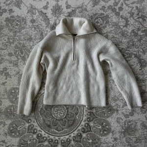 Vit ribbad stickad tröja BikBok - Vit stickad tröja från BikBok med ribbad struktur och hög krage. Tröjan har en half zip-dragkedja framtill och långa ärmar. 