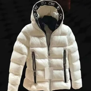 Vit pufferjacka med huva från Moncler - Snygg vit pufferjacka från Moncler med svart text på huvkanten. Jackan har två svarta dragkedjefickor framtill och en rejäl huva. Perfekt för kalla dagar och ger en clean, modern look.