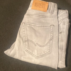 Ljusgrå slim jeans från Jack & Jones - Snygga ljusgrå slim fit jeans från Jack & Jones med klassisk femficksdesign och diskret broderad bakficka. Jeansen har en modern passform och är tillverkade i mjukt bomullsmaterial med stretch för extra komfort.