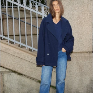 Mörkblå kappa - Säljer en mörkblå skepparkavaj med dubbelknäppning och breda slag. Jackan har en loose passform, långa ärmar med knappar vid ärmslut och är tillverkad i en ullmix. Perfekt för dig som gillar en klassisk men chill stil. Från Nelly. 