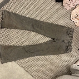 Grå bootcut jeans med svarta detaljer - Grå jeans med bootcut-modell och svarta detaljer på bakfickan. Klassisk femficksdesign och bälteshällor. Jeansen har en tvättad look och är tillverkade i ett mjukt bomullsmaterial. Perfekta för dig som gillar en avslappnad men trendig stil.