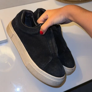 Svarta sneakers från Eytys i mocka - Säljer ett par svarta Eytys sneakers i mocka med chunky vit sula och lila detaljband baktill. Skorna har en minimalistisk design utan snörning och Eytys-logga på hälen. Perfekta för dig som gillar stilrena och trendiga sneakers. Skorna har lite skavanker därav billigt pris. Fungerar fläckfritt för mig.