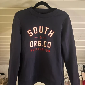 Mörkblå sweatshirt från Gina Tricot - Mörkblå sweatshirt från Gina Tricot med tryck i vitt och rött framtill. Tröjan har rund halsringning, långa ärmar och är gjord i mjuk bomullsmix. Storlek S, inte mycket använd!