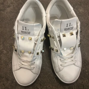 Valentino Rockstud vita och guld  - Säljer ett par vita Valentino Rockstud guld- och silverfärgade nitar. Klassisk låg modell med snörning och rund tå. Snygg och edgy detalj med nitar längs sidorna och tungan. Perfekta för dig som vill sticka ut med lyxig streetstyle. St 37, kommer med allt som på sista bilden, prisk kan diskuteras💕
