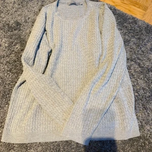 Ljusgrå stickad tröja från b.young - Säljer en ljusgrå stickad tröja från b.young i storlek XL. Tröjan har ett diskret strukturmönster, rund halsringning och långa ärmar. Perfekt för lager-på-lager och chill höst- eller vinterstil.