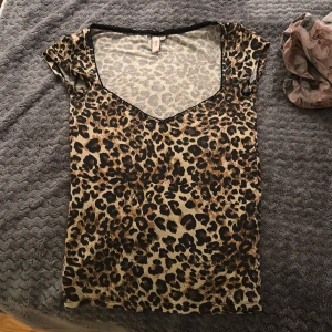 Leopardmönstrad topp från Nelly XS - Säljer en snygg leopardmönstrad topp från Nelly i storlek XS. Toppen har v-ringning med svart spetskant och är kortärmad. Färgerna går i beige, brunt och svart och materialet känns mjukt och stretchigt, troligen polyester eller bomull.